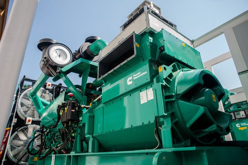 A powerful green Cummins diesel generator with prominent exhaust pipes and cooling fans, likely used for industrial power generation.





