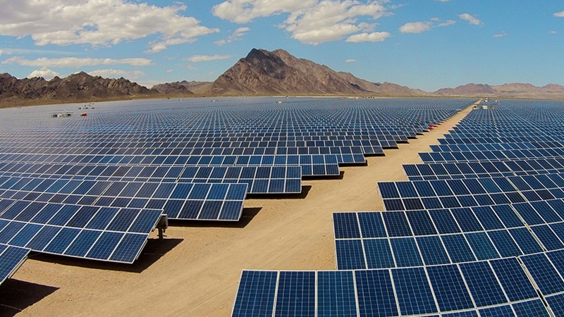 A vast photovoltaic power station with rows of solar panels stretching toward a distant mountain range